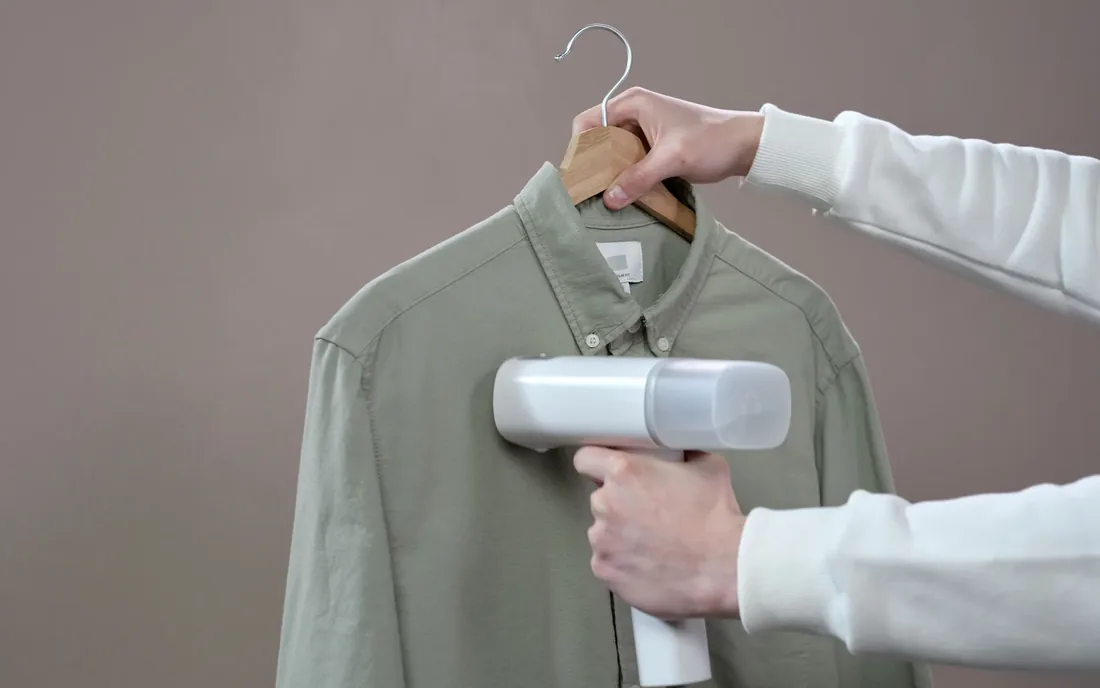 Hands steaming a finished shirt on a hanger
